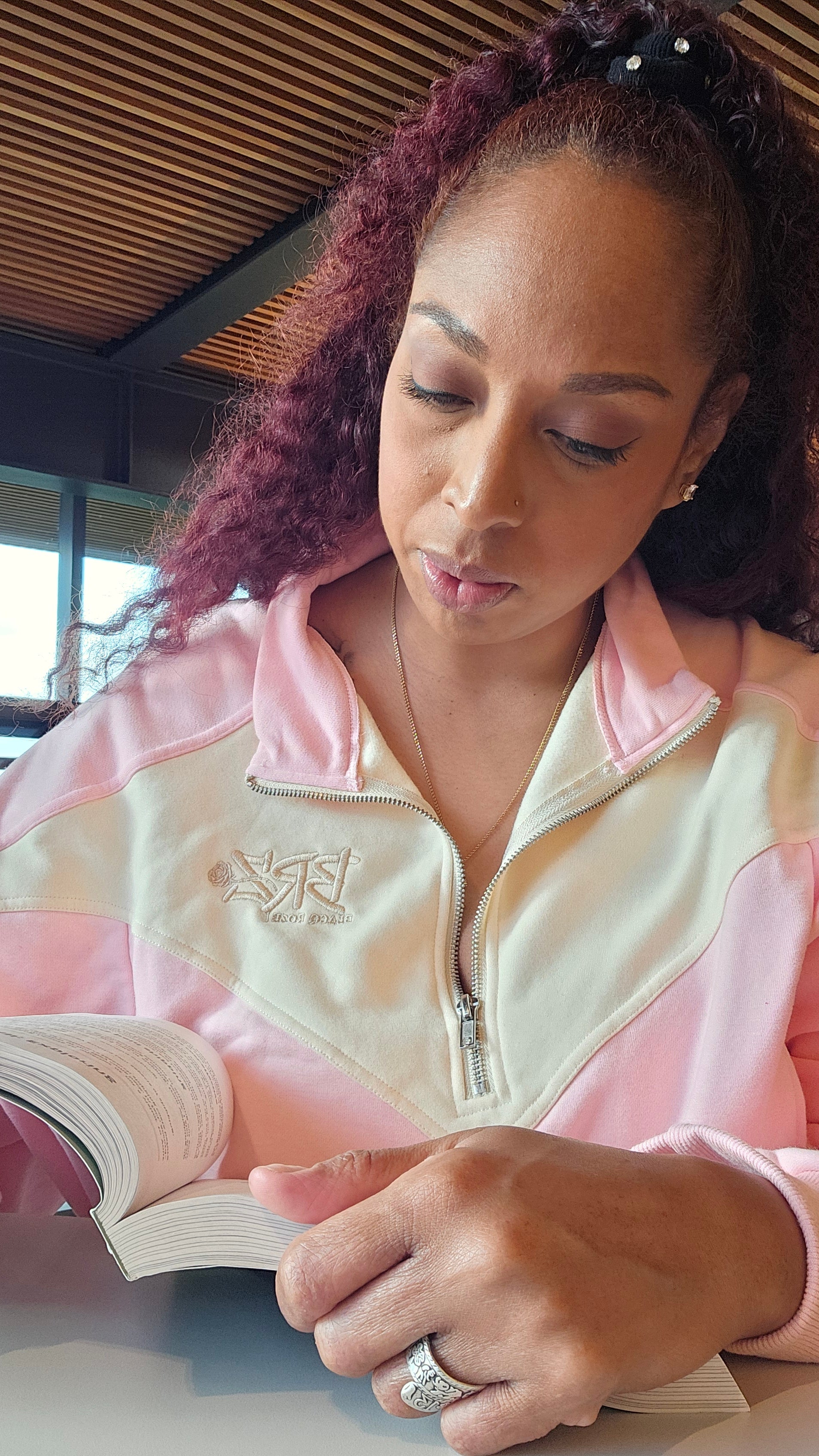 Woman in pink satin robe holding a book, sitting on a couch.